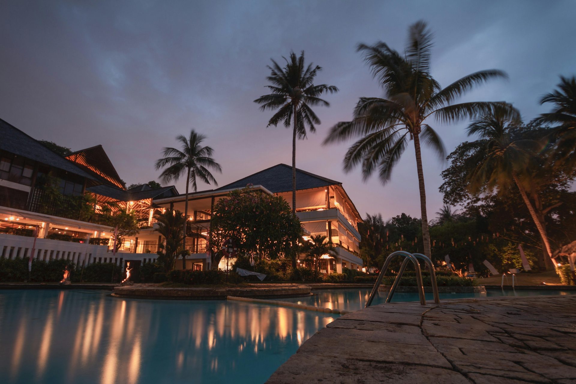Luxuriöses tropisches Resort mit Swimmingpool und Palmen in der Abenddämmerung, perfekt für einen ruhigen Urlaub.